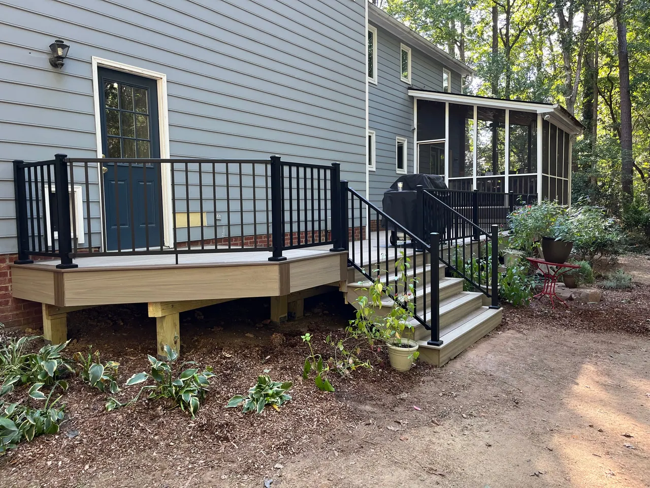 Wood deck with black aluminium railing and stairs beside a navy entry door