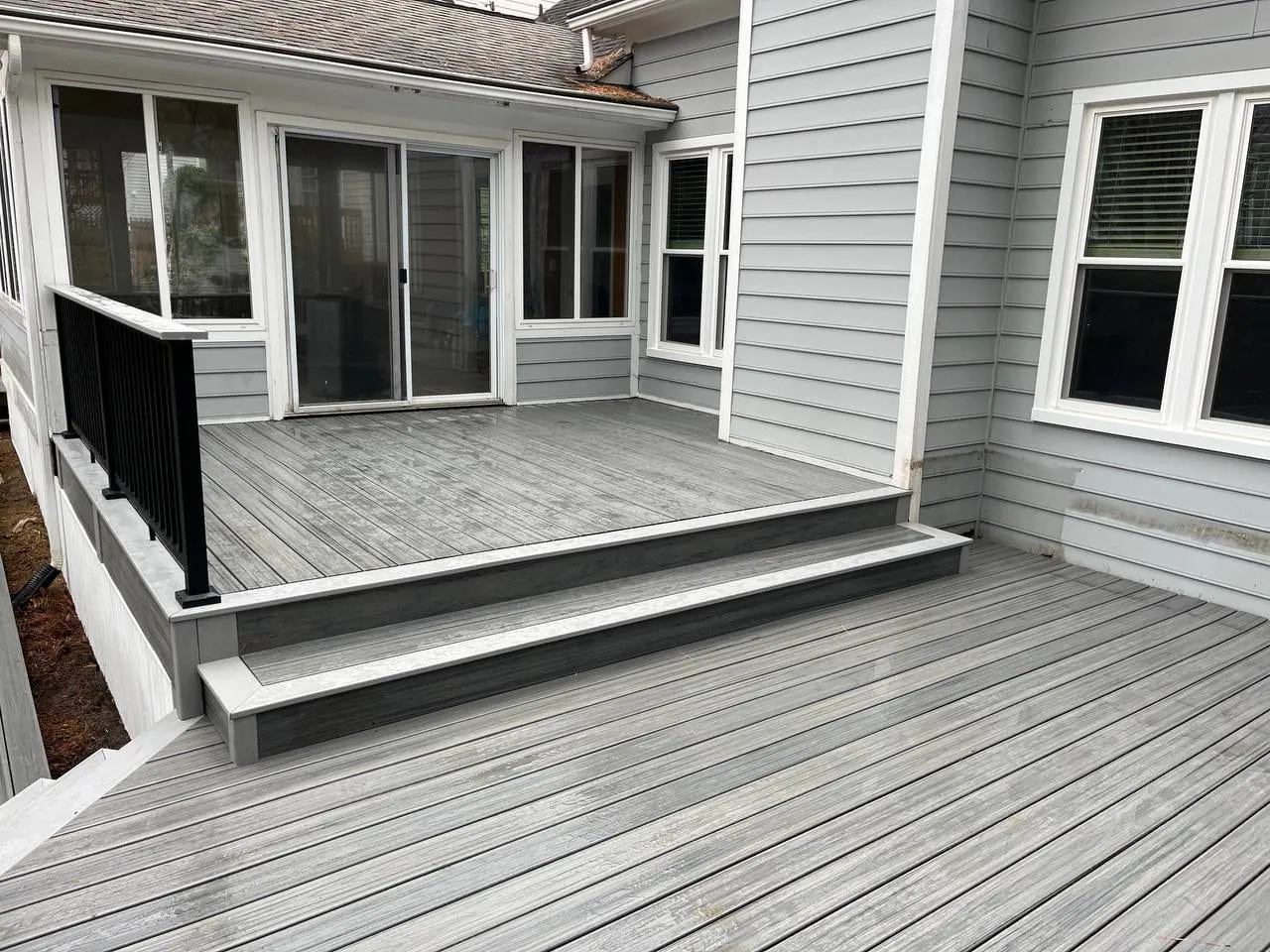 Grey composite deck platform with a single step down, black railing and sliding doors to the house