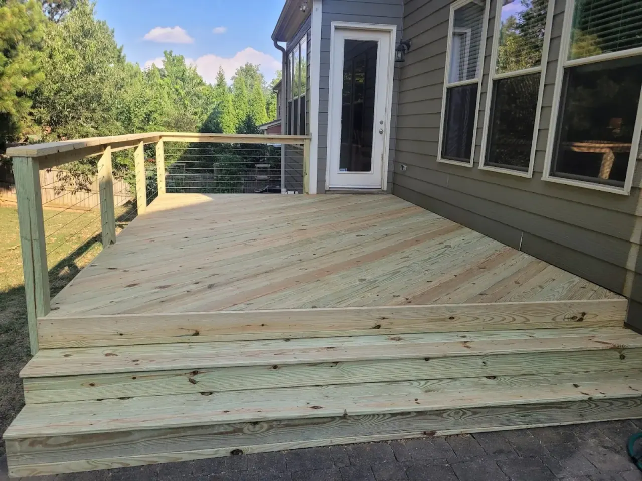 Newly built pressure-treated deck with horizontal cable railing under a clear sky
