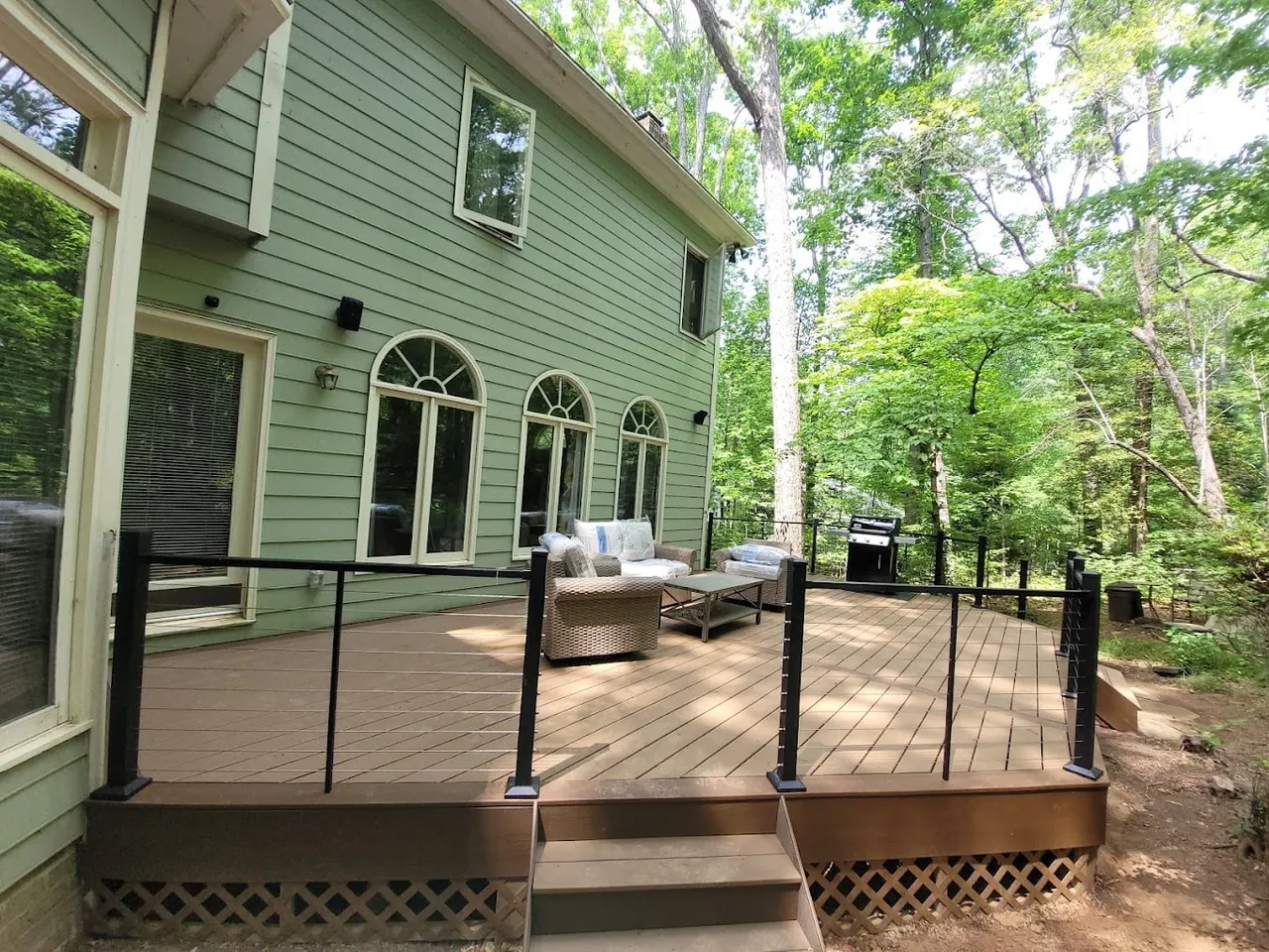Deck with black cable railing and lounge seating behind a sage-green home with arched windows