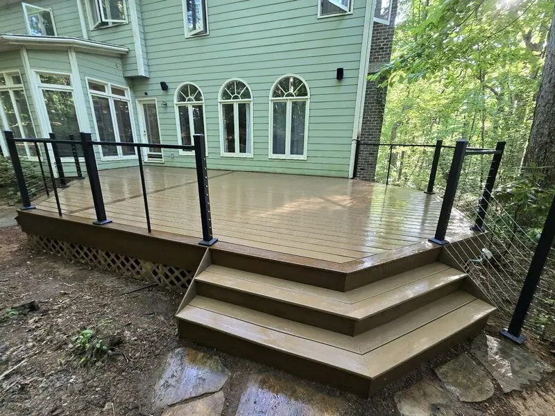 Honey-toned deck with black cable railing and wide cascading steps down to a stone landing behind a sage-green home