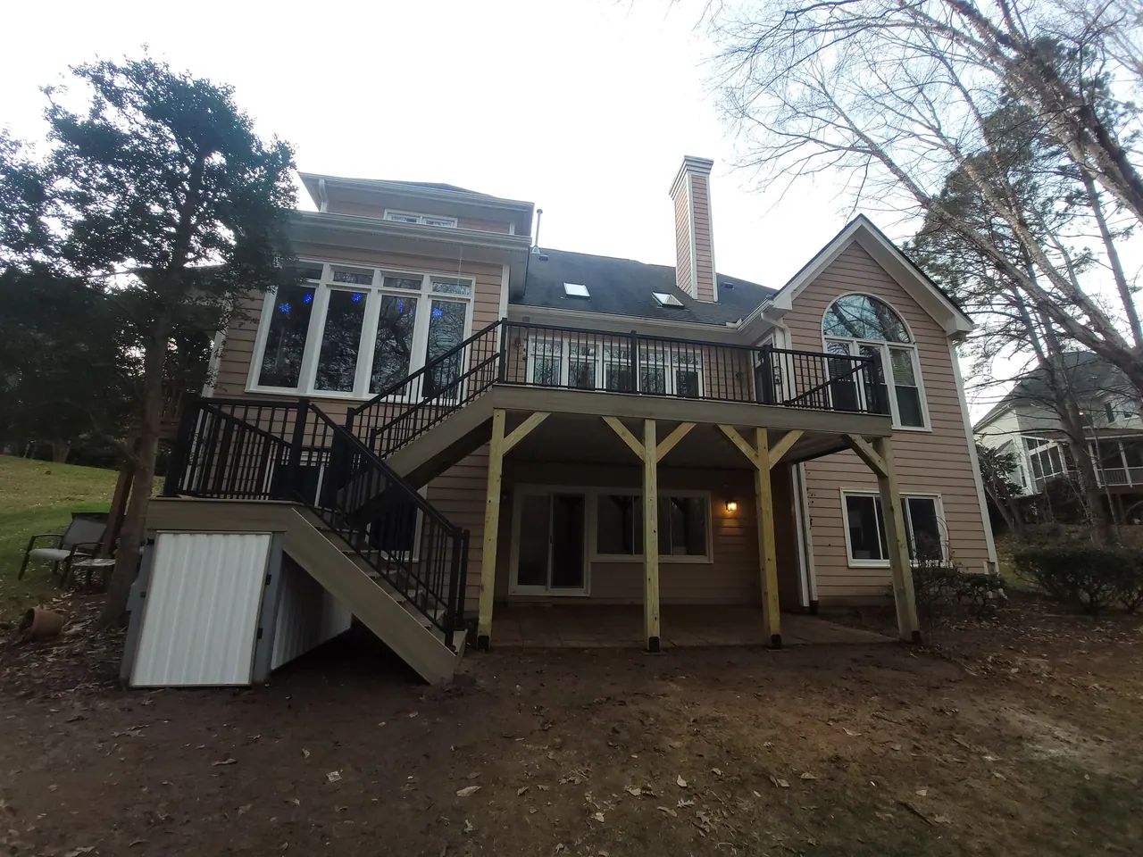 Elevated deck on timber posts with black aluminum railing and stairs down to a paver patio
