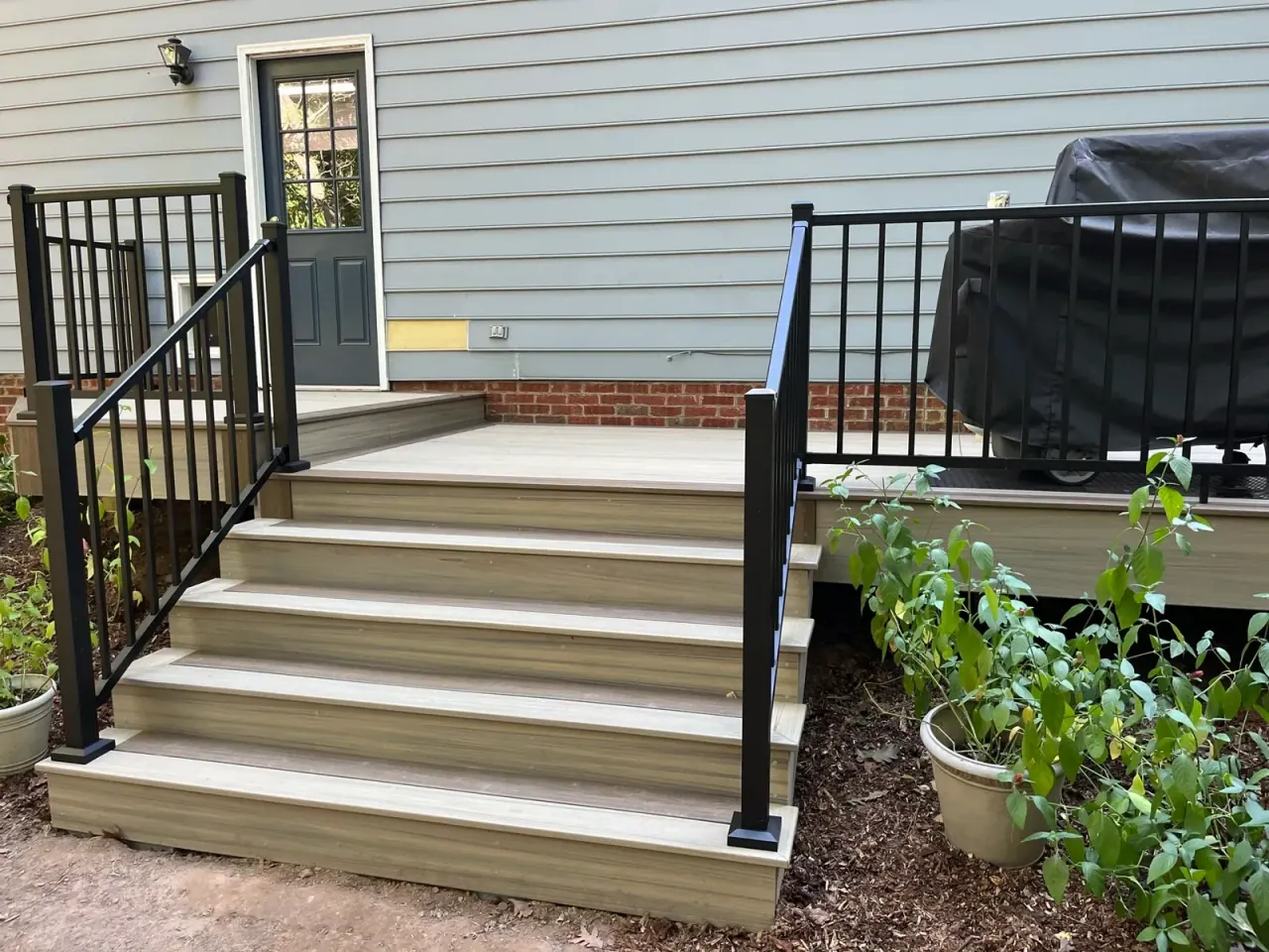 Composite deck stairs with black aluminum railing leading to a brick home entry