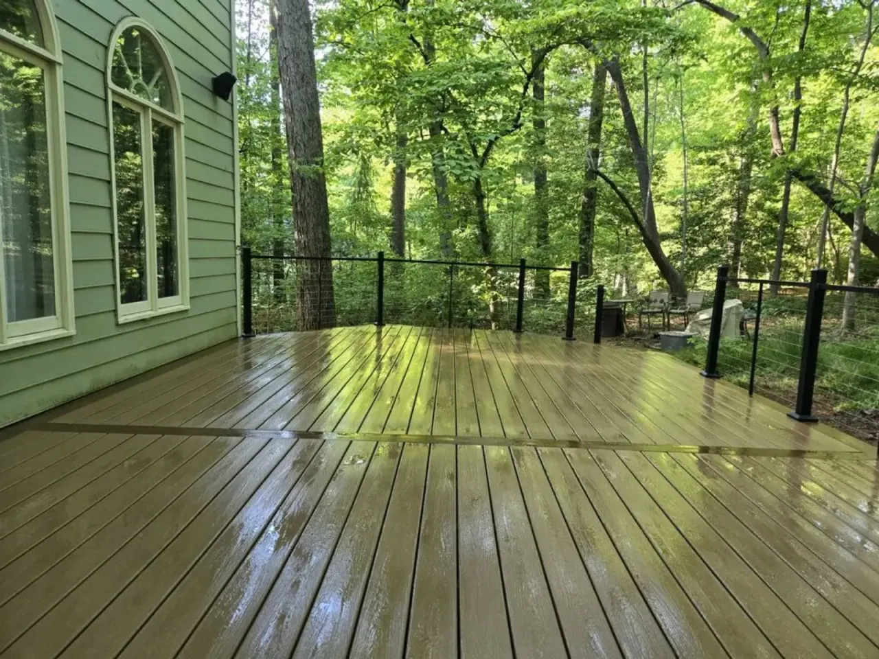 Freshly stained wood deck with black railing under spring tree canopy