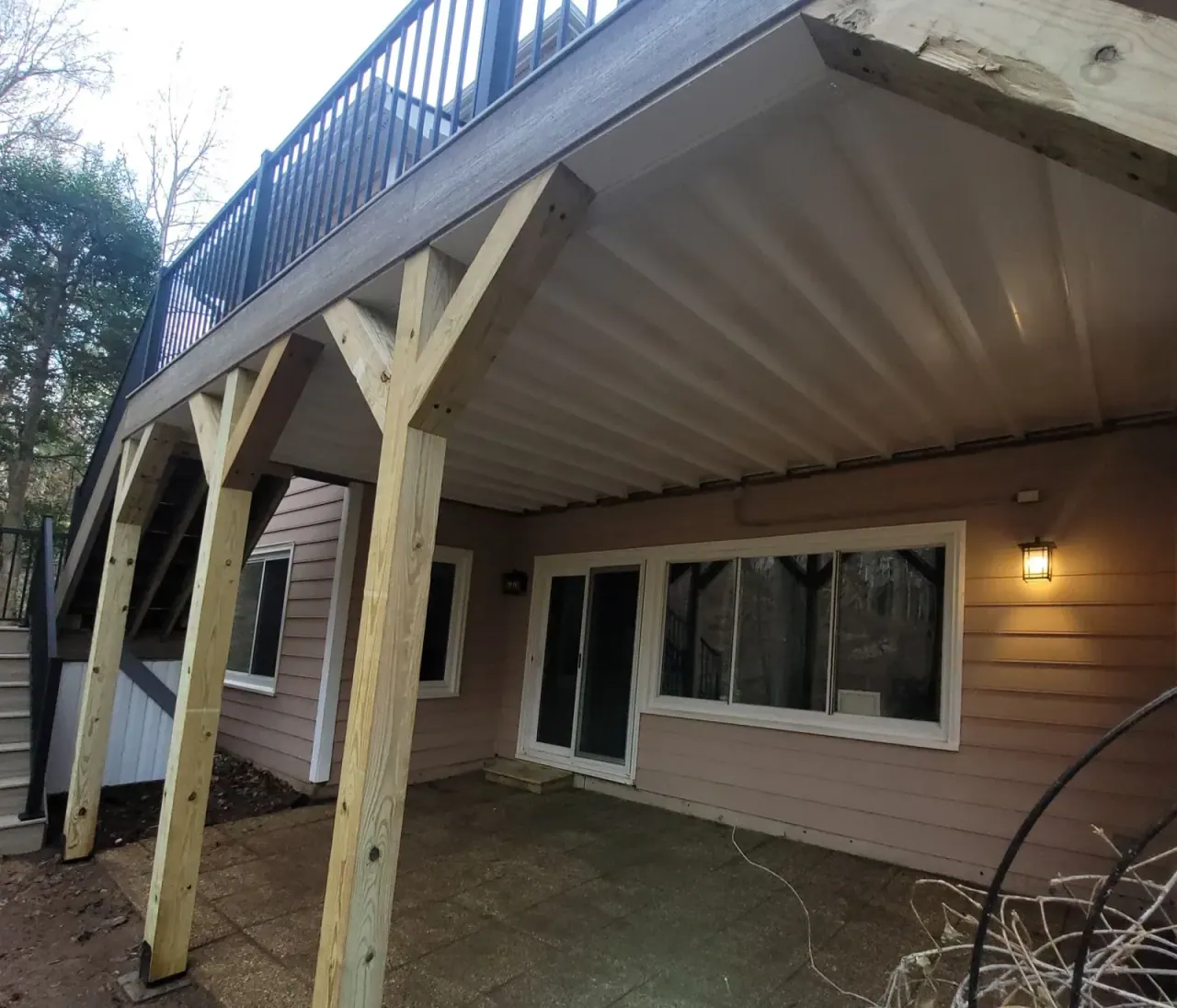 Covered outdoor living space beneath an elevated deck with timber posts and finished ceiling