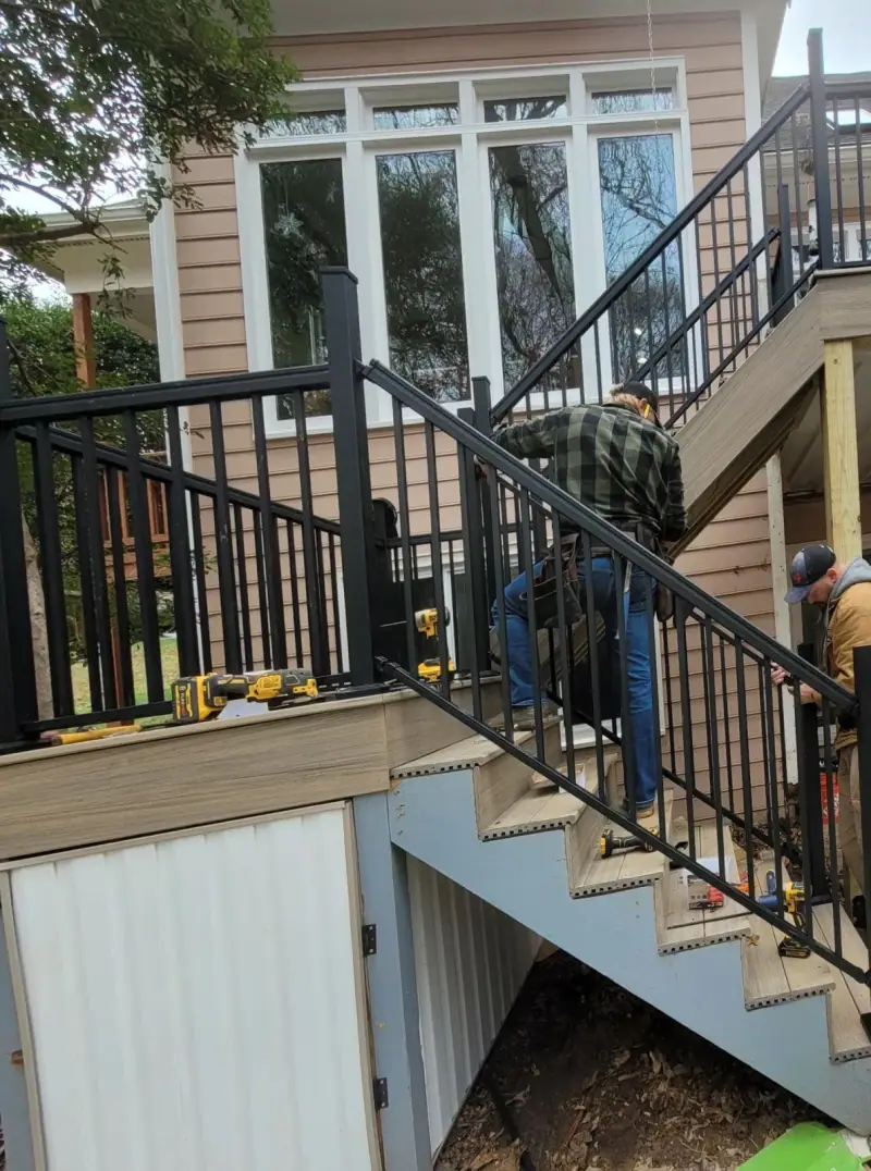 Black aluminum stair railing leading down past an under-deck storage enclosure