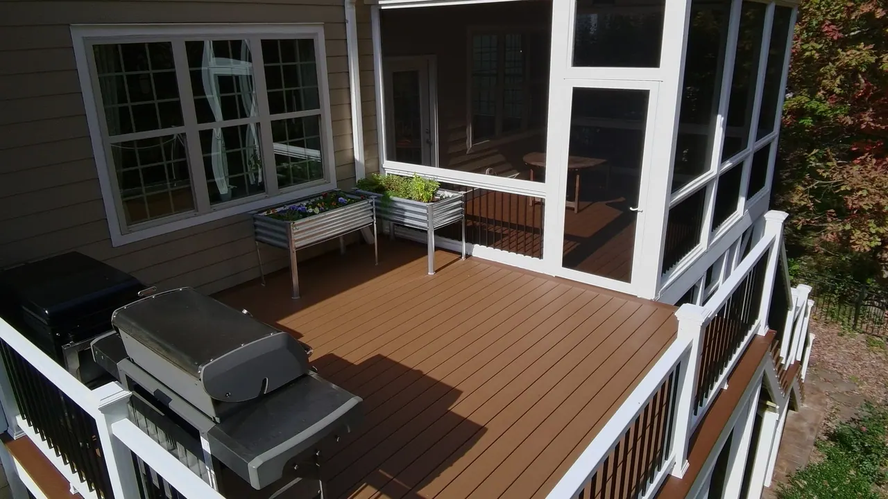 Screened porch beside a brown composite deck with a grill station and raised planters