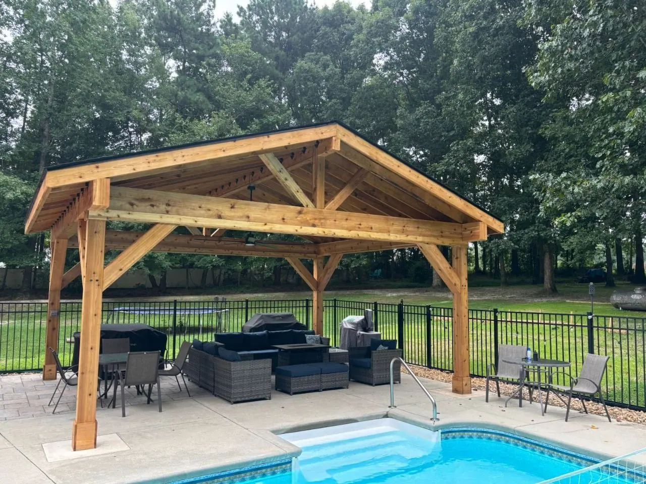 Timber pavilion with a gabled roof beside a backyard pool and patio seating