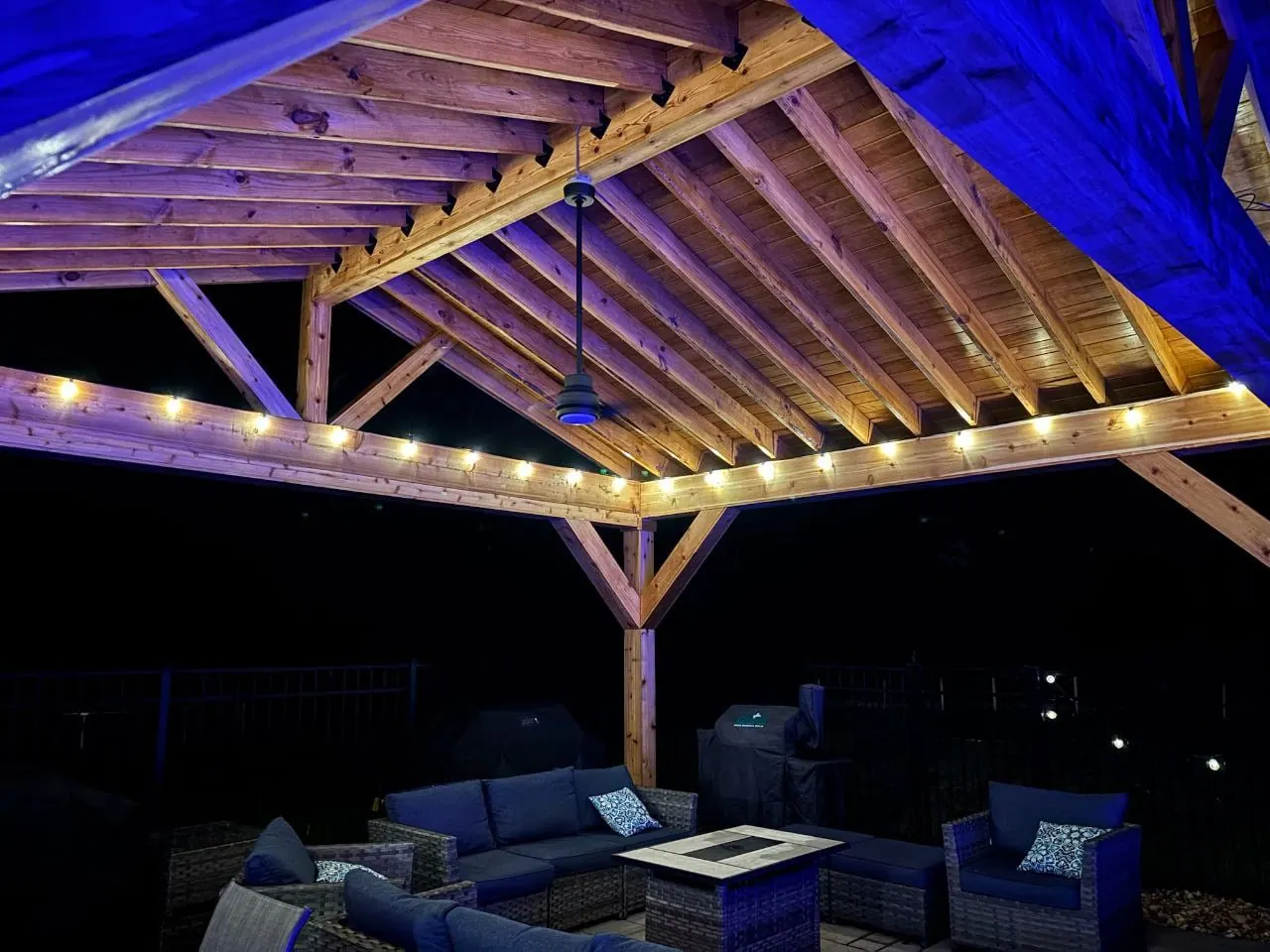 Underside of a timber pavilion at night, rafters lit with warm strip lighting and blue accent light